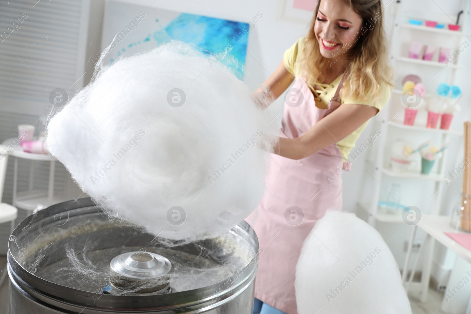 Photo of Young woman making cotton candy using modern machine in room