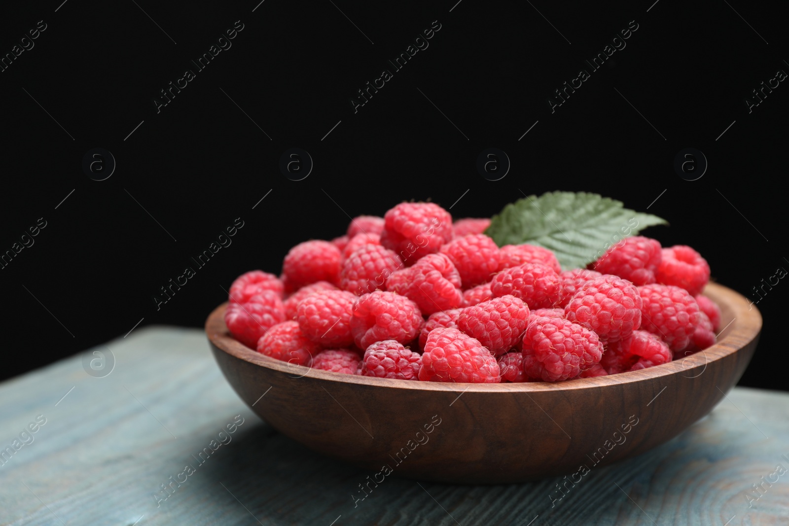 Photo of Delicious fresh ripe raspberries in plate on blue wooden table