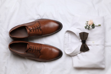 Photo of Wedding shoes and shirt on white fabric, flat lay