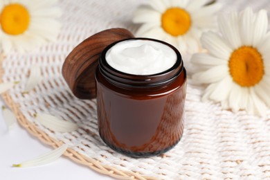 Photo of Glass jar of face cream and beautiful flowers on white table