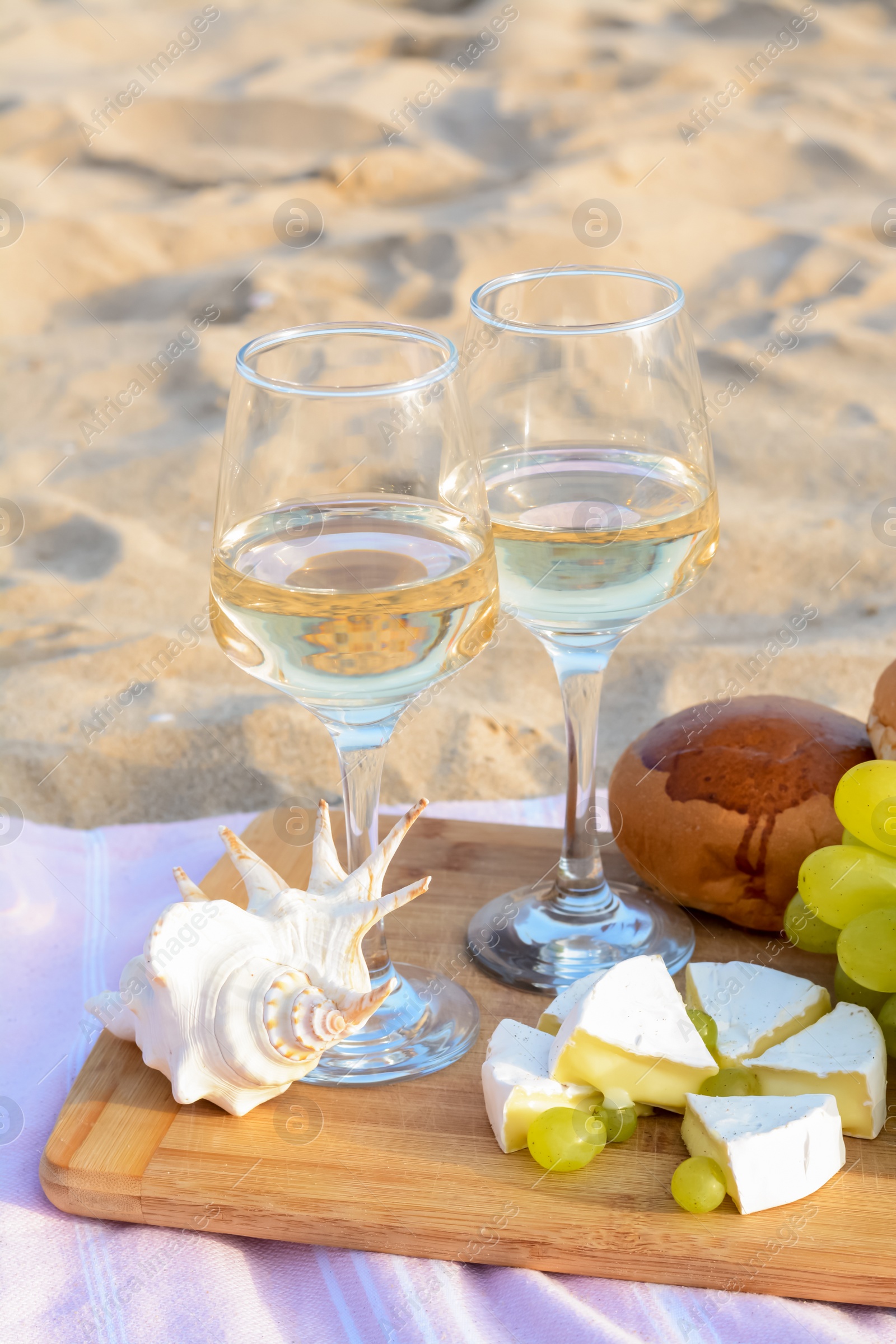 Photo of Glasses with white wine and snacks for beach picnic on sand outdoors