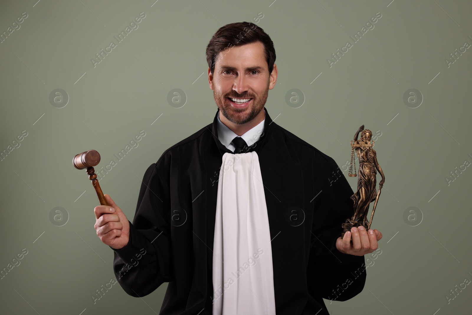 Photo of Happy judge with gavel and figure of Lady Justice on green background