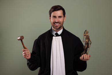 Photo of Happy judge with gavel and figure of Lady Justice on green background