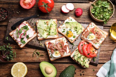 Different delicious sandwiches with microgreens on wooden table, flat lay