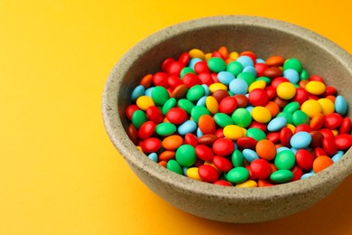 Photo of Bowl with tasty colorful candies on yellow background, closeup