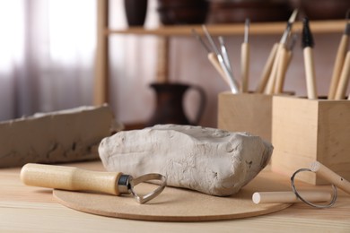 Photo of Clay and set of modeling tools on wooden table in workshop