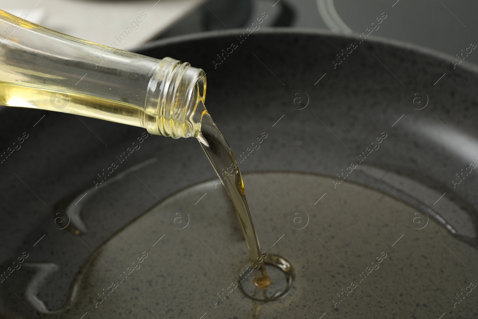 Photo of Pouring cooking oil from bottle into frying pan, closeup