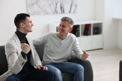 Photo of Blurred view of happy men talking while sitting on sofa at home