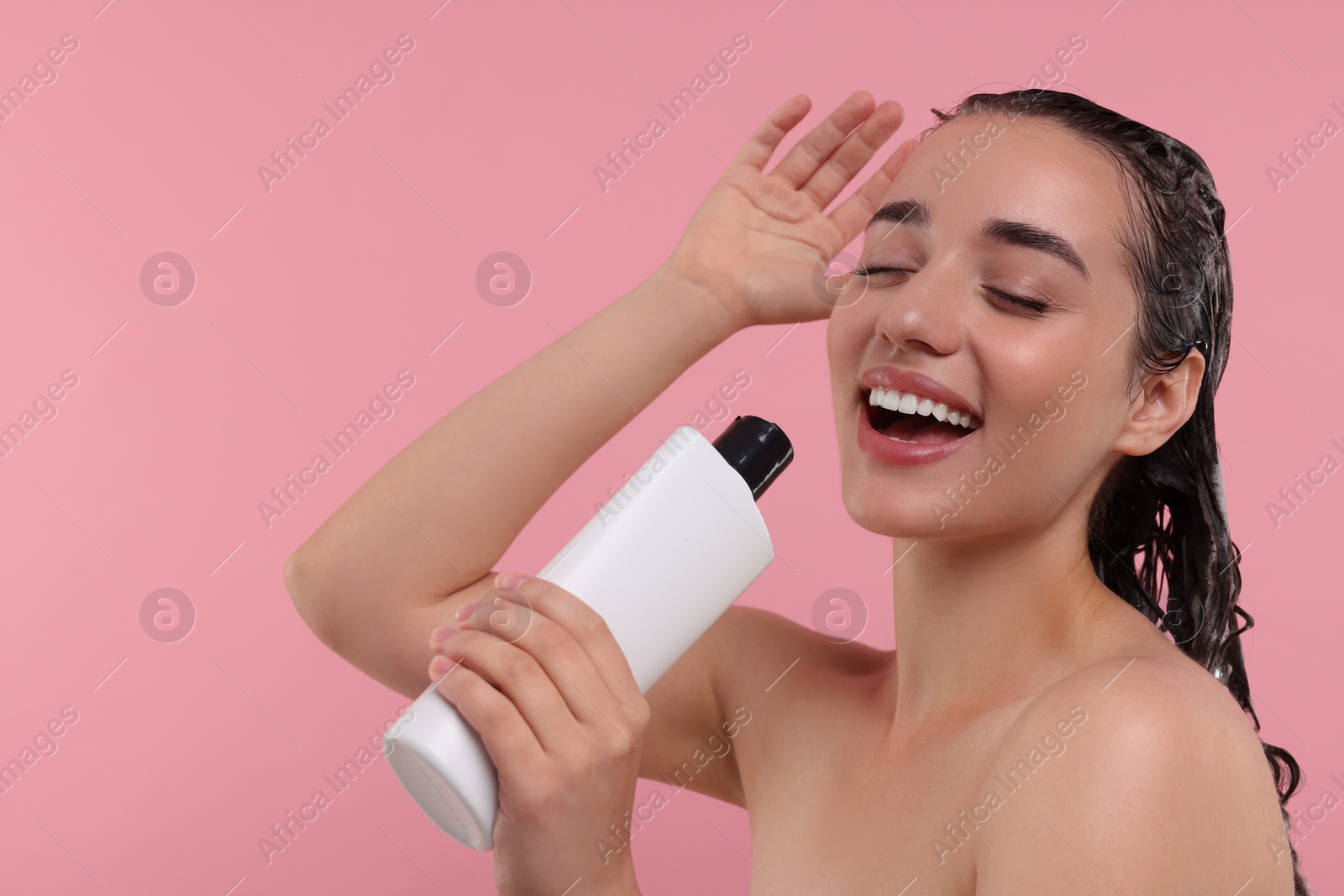 Photo of Washing hair. Portrait of beautiful happy woman with bottle singing on pink background. Space for text