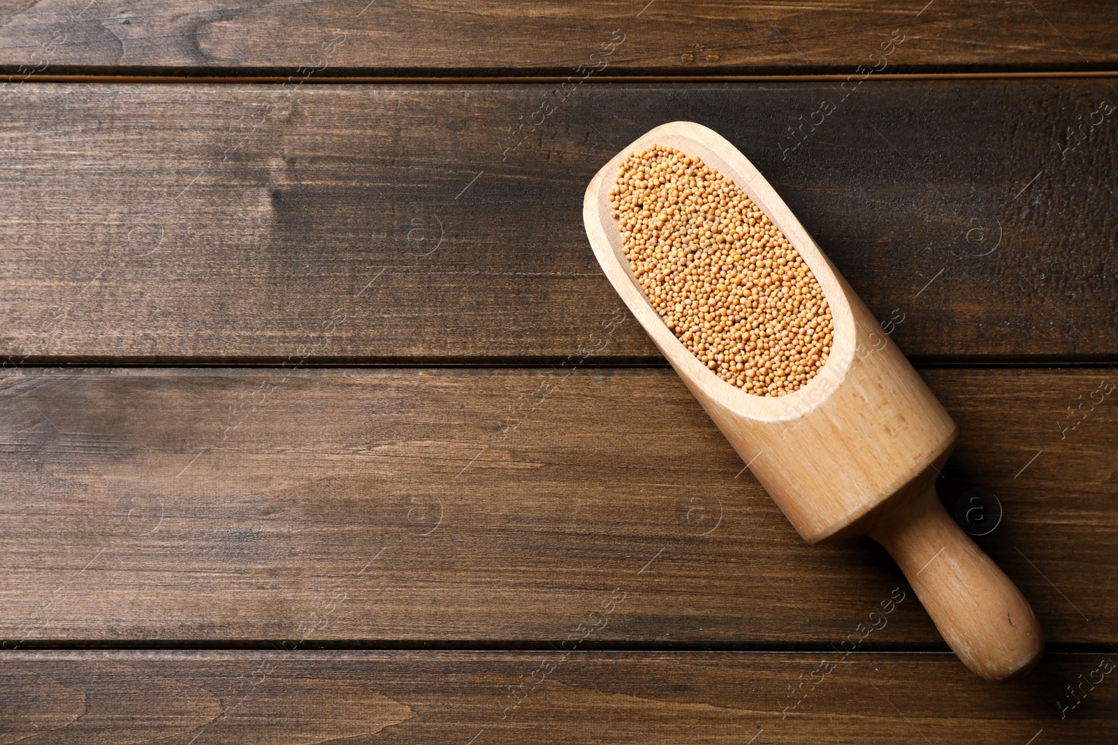 Photo of Mustard seeds in scoop on wooden table, top view. Space for text