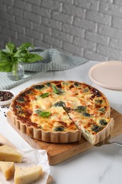 Taking piece of delicious homemade quiche with salmon and broccoli from wooden board on white table