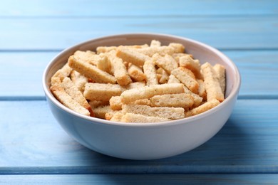 Photo of Crispy wheat rusks in bowl on light blue wooden table