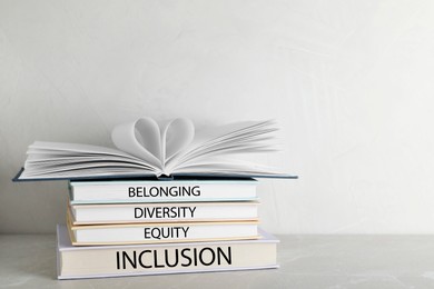 Image of Stack of hardcover books with words Belonging, Diversity, Equity, Inclusion on table against white background