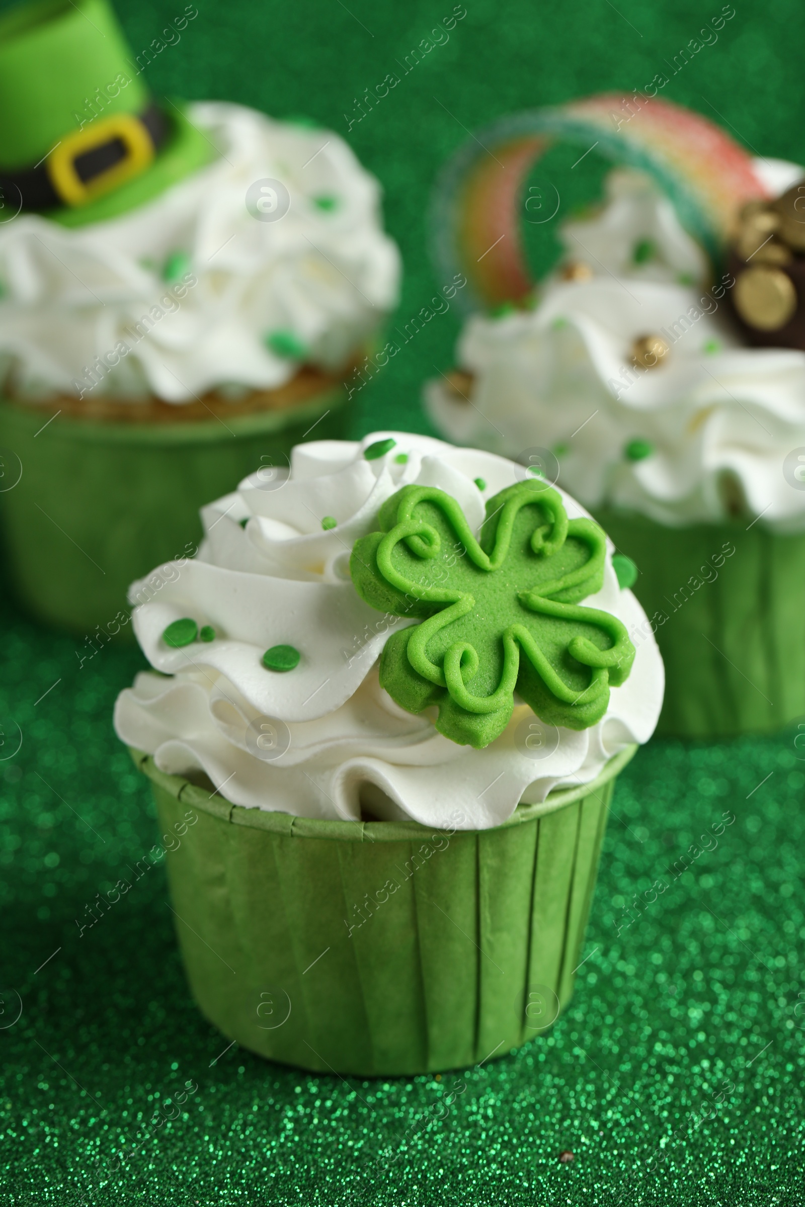 Photo of St. Patrick's day party. Tasty festively decorated cupcakes on shiny green surface, closeup