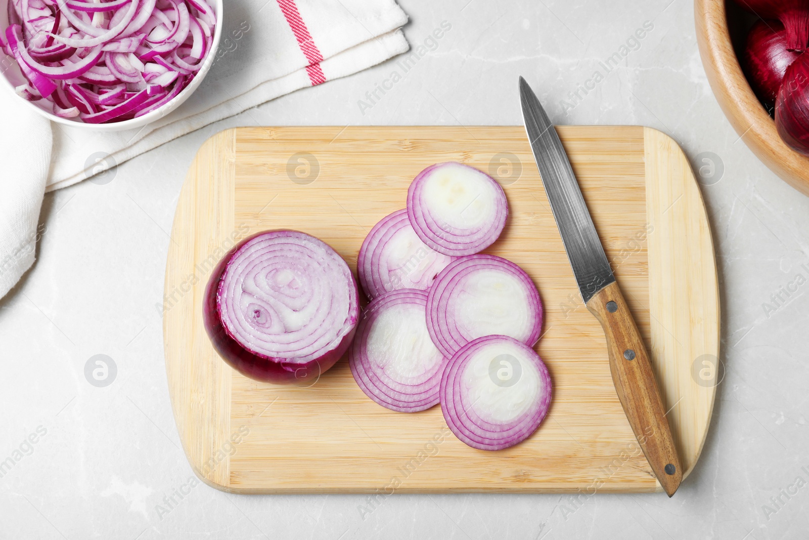 Photo of Wooden board with cut fresh red onion and knife on marble table, flat lay