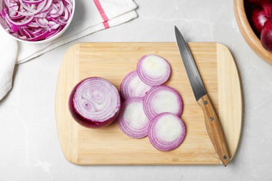 Photo of Wooden board with cut fresh red onion and knife on marble table, flat lay