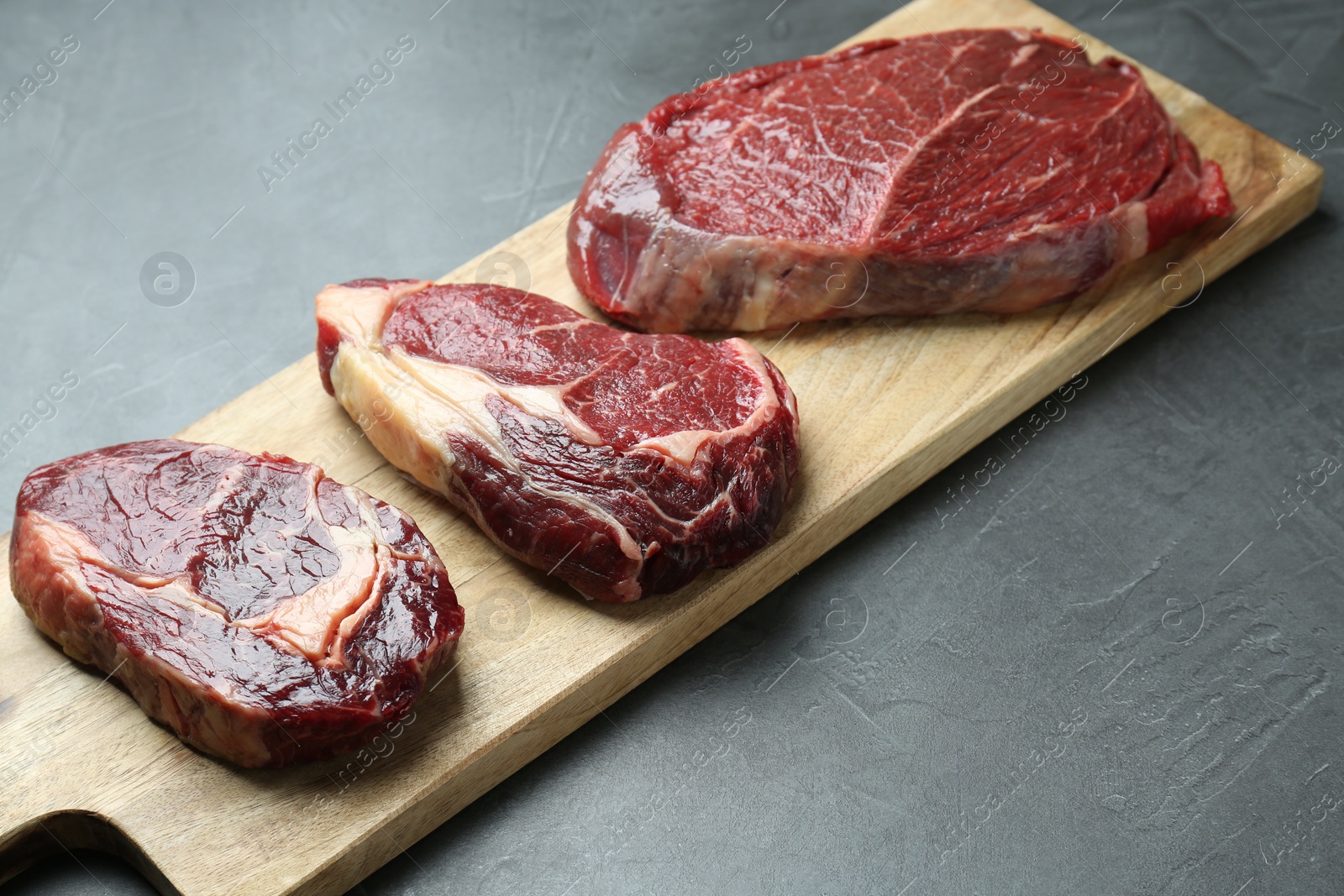 Photo of Wooden board with pieces of raw beef meat on grey table