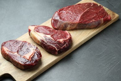 Photo of Wooden board with pieces of raw beef meat on grey table