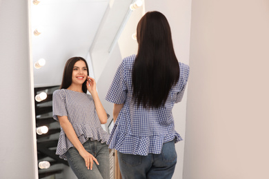 Photo of Young attractive woman looking at herself in stylish mirror at home