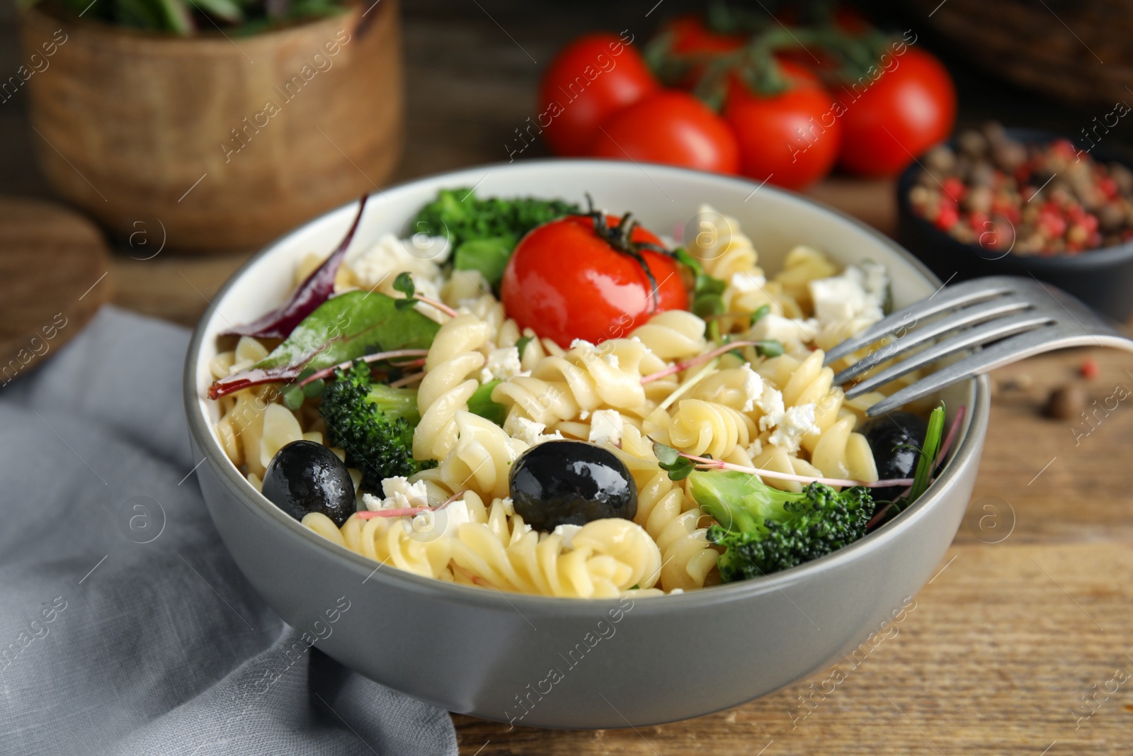 Photo of Bowl of delicious pasta with tomatoes, olives and broccoli on wooden table, closeup