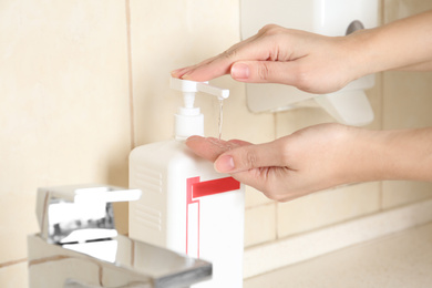 Photo of Woman applying antiseptic gel on hand in public bathroom, closeup