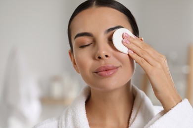 Beautiful woman removing makeup with cotton pad indoors