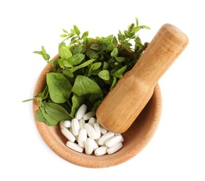 Mortar with fresh green herbs and pills on white background, top view