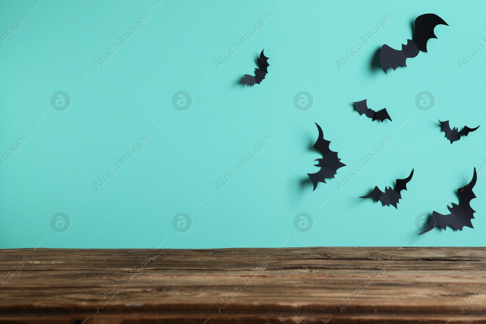 Photo of Empty wooden table near light blue wall decorated with paper bats, space for text. Halloween celebration