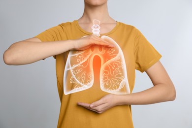 Woman holding hands near chest with illustration of lungs on light grey background, closeup