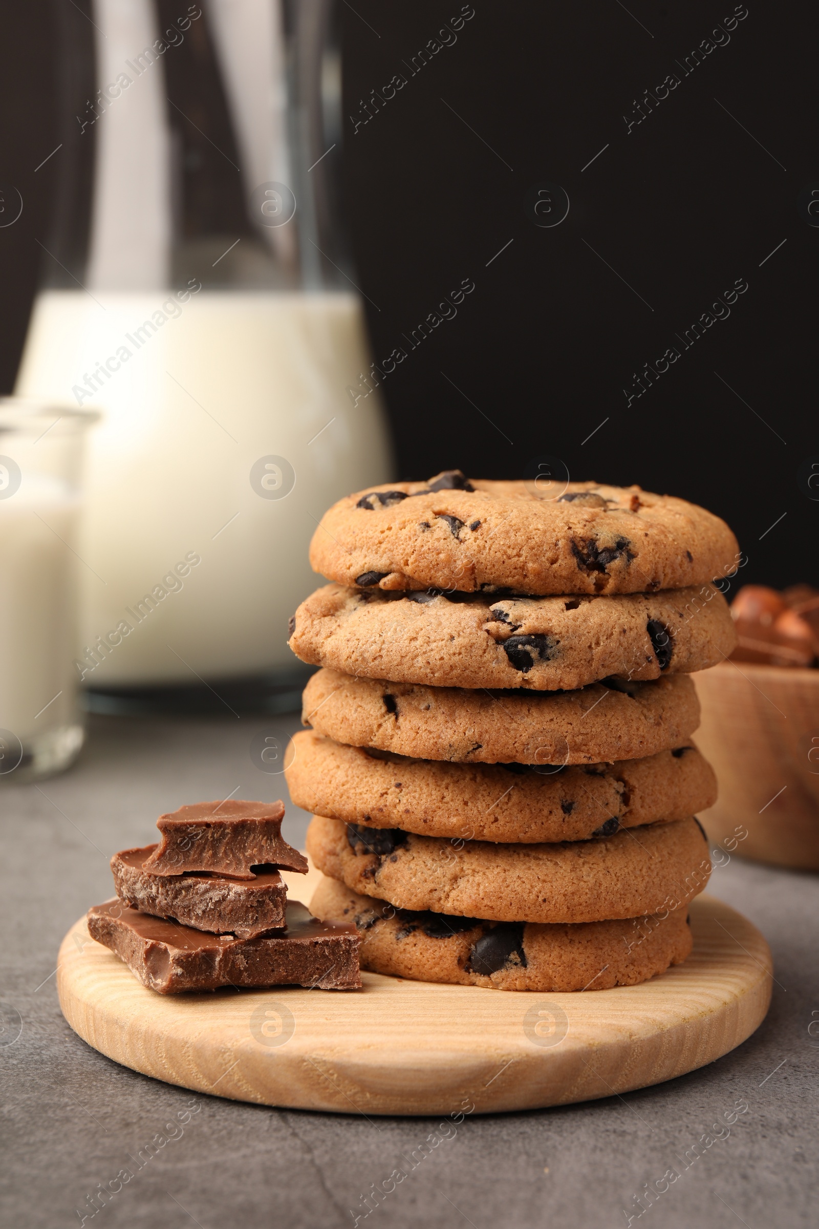 Photo of Stack of delicious chocolate chip cookies and milk on grey table