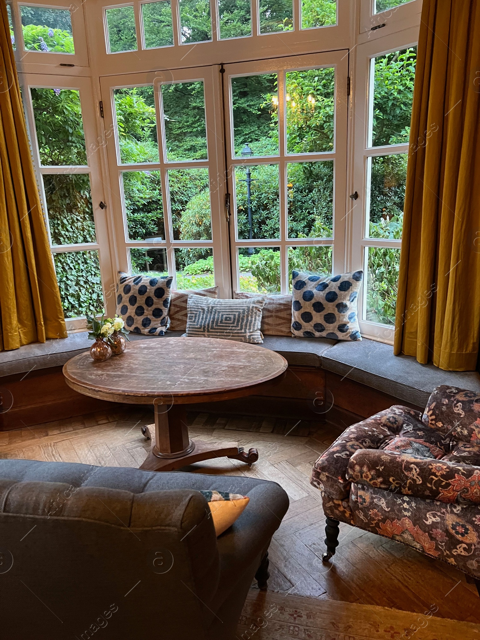 Photo of Wooden table near bay window seat with cushions in cozy room. Interior design