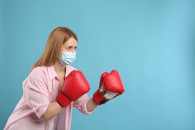 Photo of Woman with protective mask and boxing gloves on light blue background, space for text. Strong immunity concept