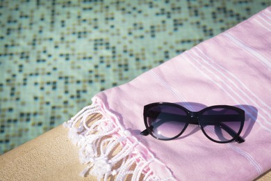 Stylish sunglasses and blanket near outdoor pool on sunny day, space for text