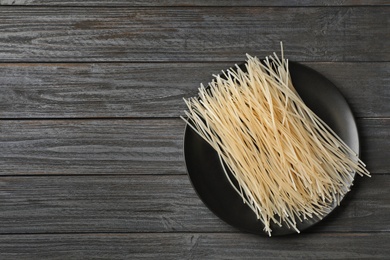 Photo of Plate with raw rice noodles on wooden background, top view. Space for text