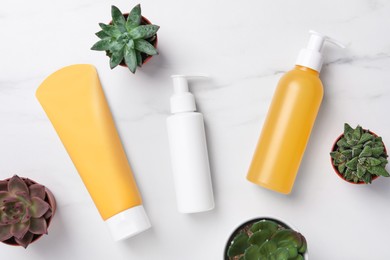 Photo of Different face cleansing products and potted succulents on white marble table, flat lay