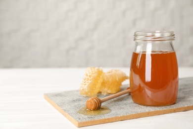Photo of Jar of tasty fresh honey and dipper on board