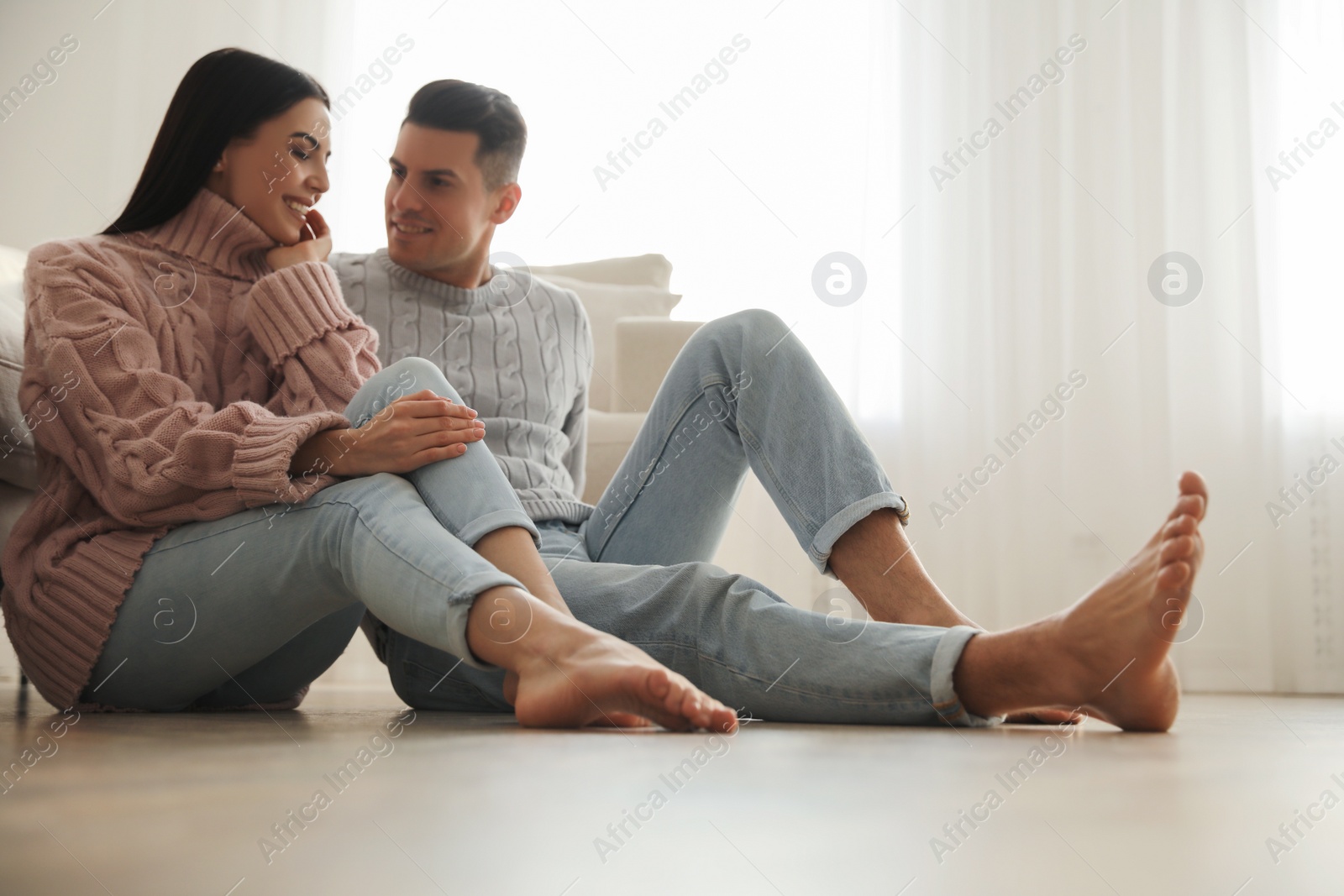 Photo of Happy couple sitting on warm floor in living room. Heating system