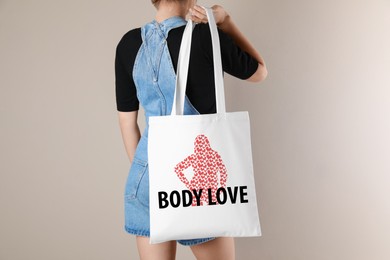 Woman holding bag with words Body Love and female figure made of hearts near light wall, closeup