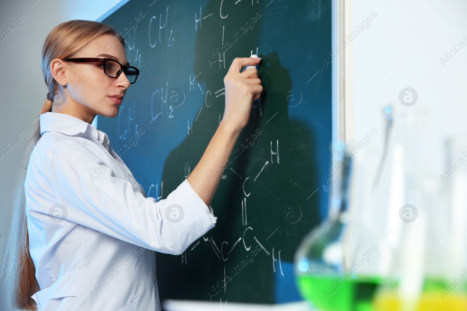 Photo of Female scientist writing chemical formula on chalkboard indoors