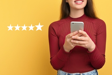 Image of Woman leaving review online via smartphone on yellow background with five stars, closeup. Service or product feedback