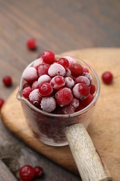 Frozen red cranberries in glass pot on wooden table, closeup