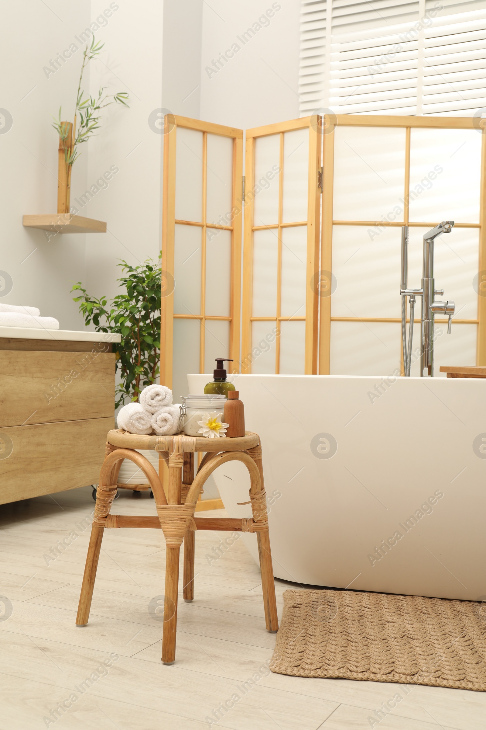 Photo of Different spa products on wicker table near ceramic tub in bathroom