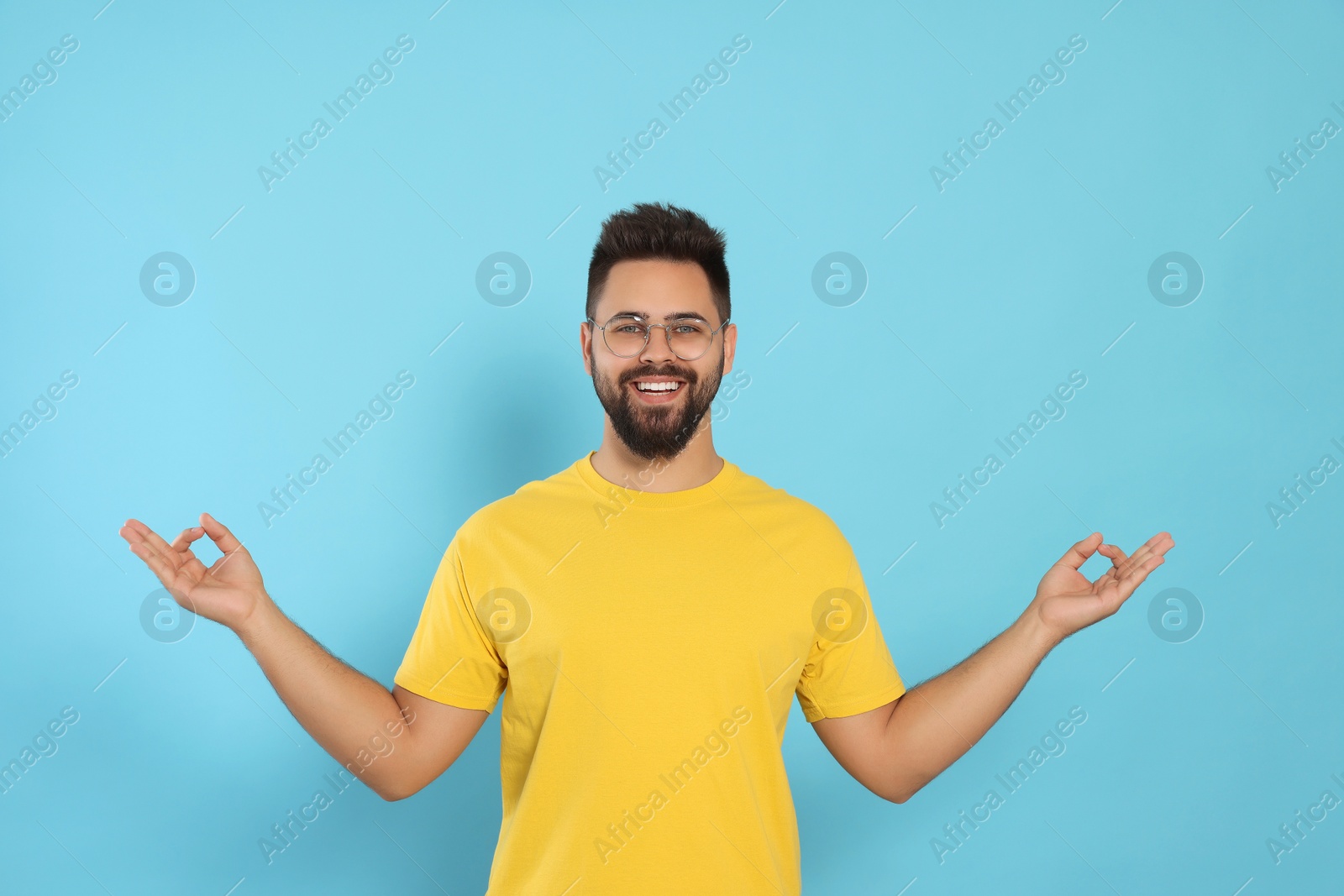 Photo of Young man meditating on light blue background. Zen concept
