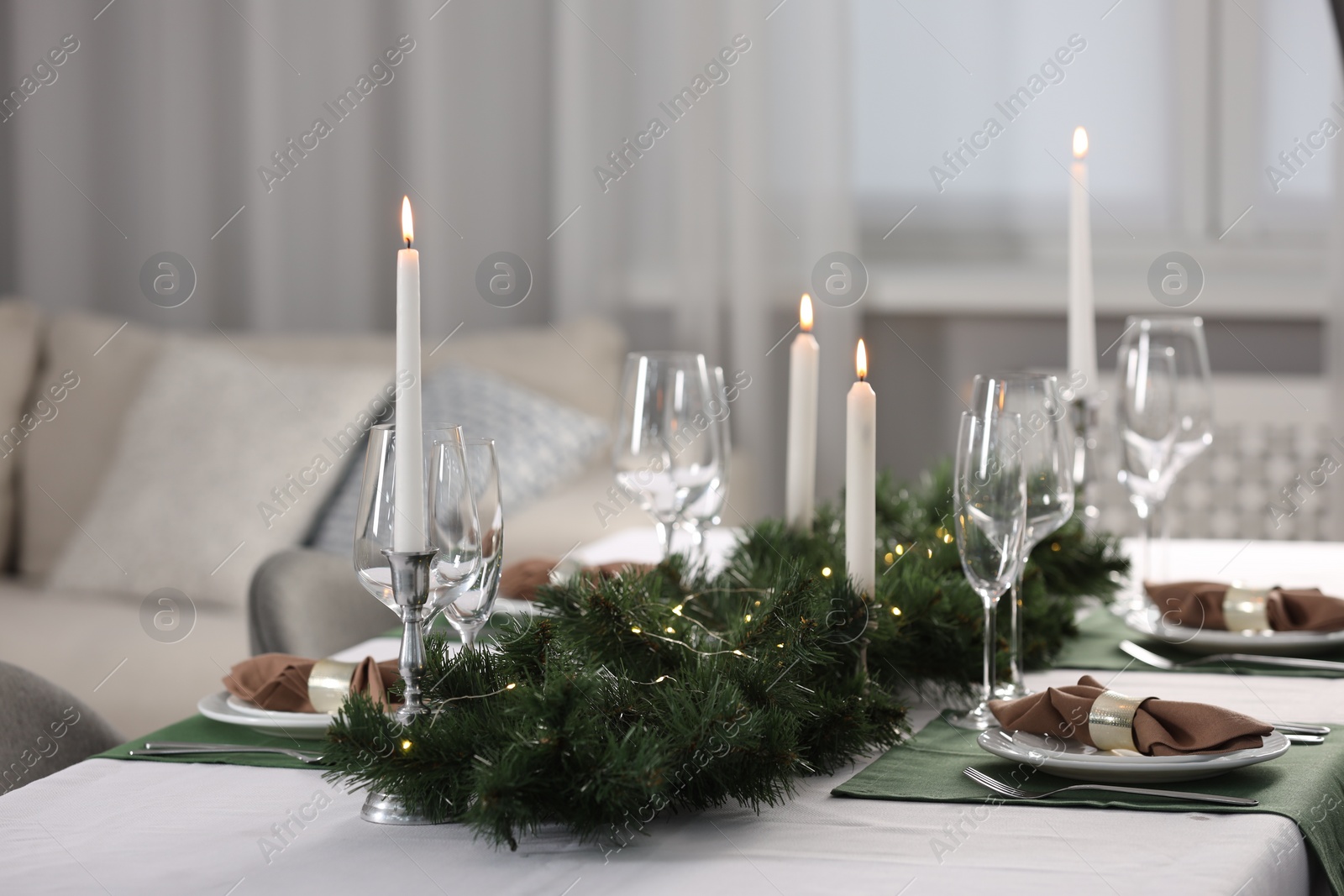 Photo of Christmas table setting with burning candles and festive decor in room