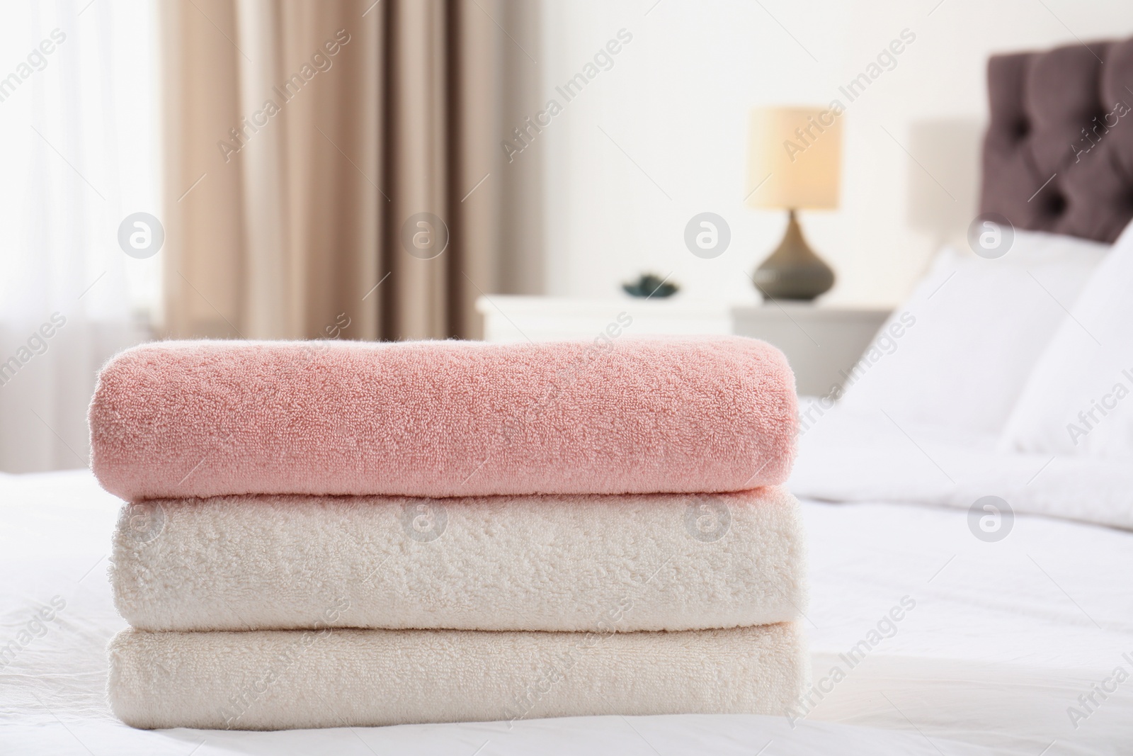 Photo of Stack of folded soft towels on bed in room. Space for text