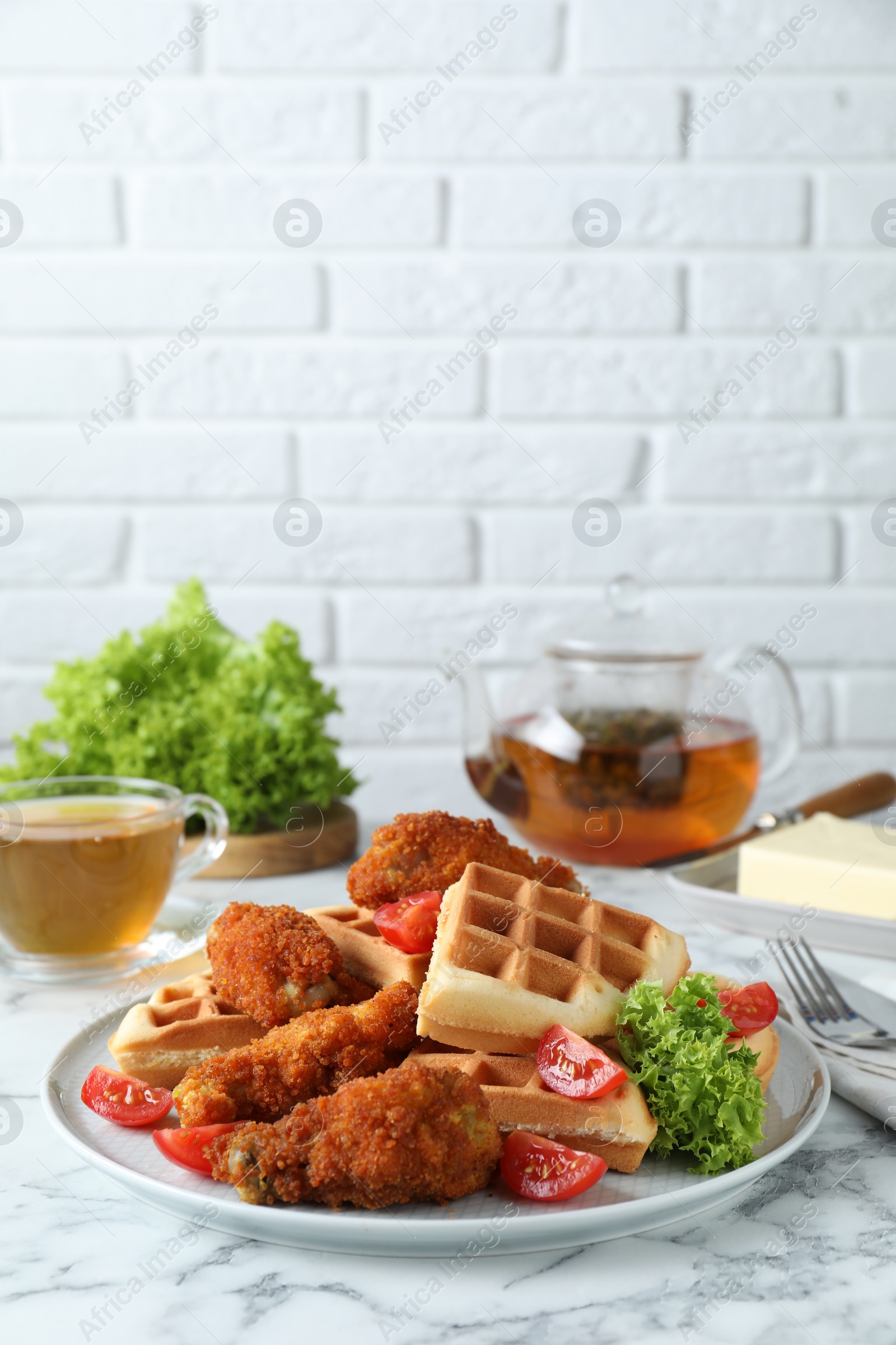 Photo of Tasty Belgian waffles served with fried chicken, tomatoes and lettuce on white marble table