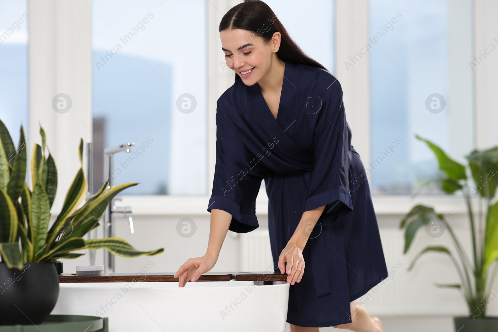 Photo of Beautiful happy woman wearing stylish bathrobe near tub in bathroom