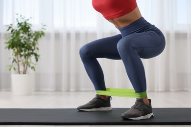 Photo of Woman doing squats with fitness elastic band on mat at home, closeup. Space for text