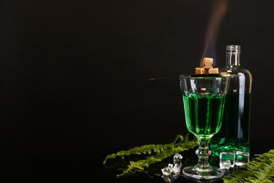 Absinthe, flaming brown sugar, ice cubes and green leaves on mirror table, space for text. Alcoholic drink