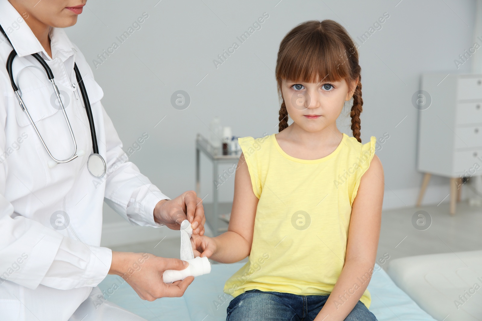 Photo of Female doctor applying bandage on little girl's finger in clinic. First aid